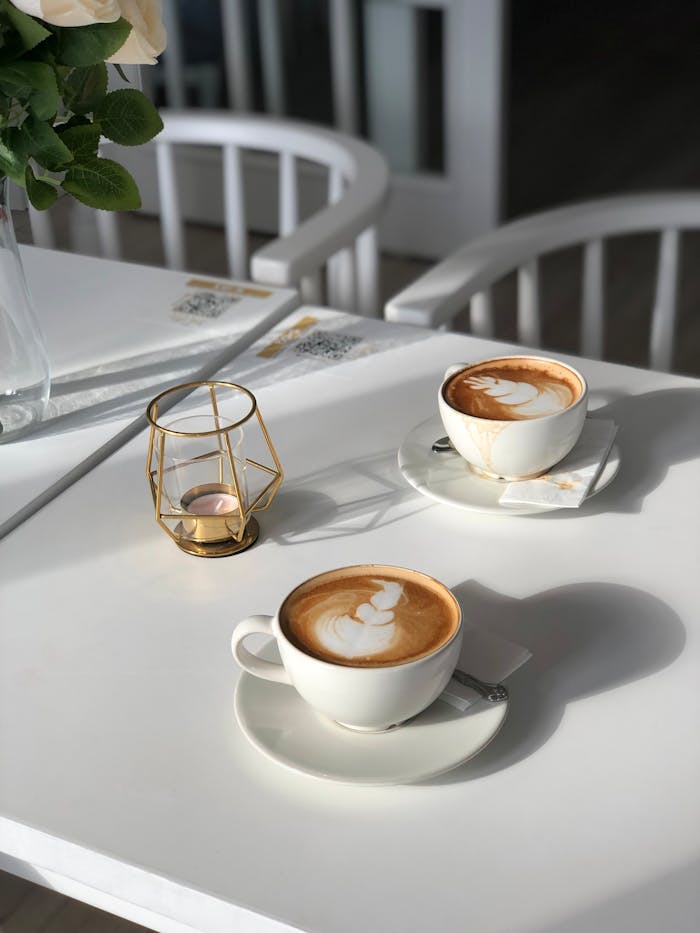 Two cappuccino cups with latte art on a white table, perfect for a cozy cafe vibe.