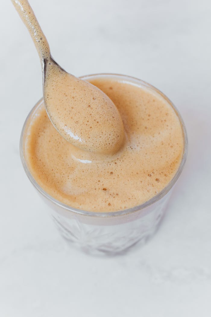 Close-up of frothy Dalgona coffee in a glass with a spoon on white background.